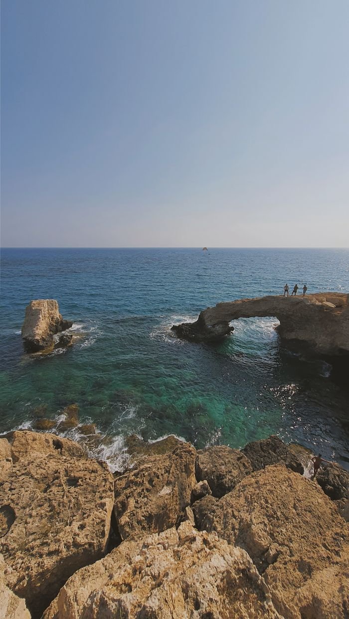 Stunning natural rock arch over the sea with clear blue skies in Cyprus, ideal for travel and nature themes.